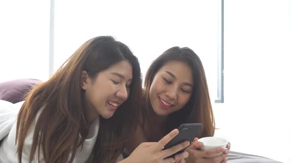 Beautiful young asian women LGBT lesbian happy couple sitting on bed hug and using phone . alt