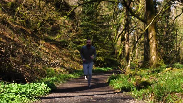 SLOW MOTION of bearded young man running up a forest then passing the camera alt