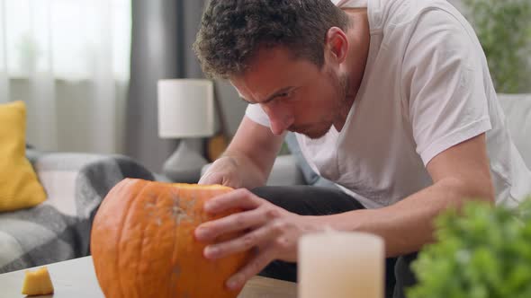 Young Man Cuts Out Jack's Lantern with a Knife at Home alt