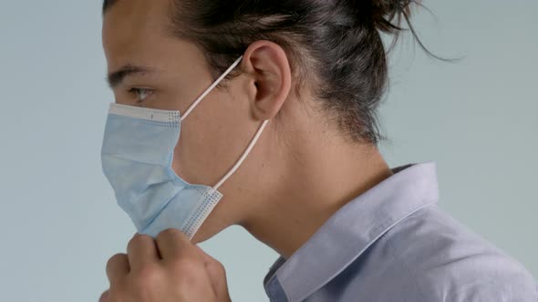 Left Profile of Adult Male with Long Hair Wearing Button Down Shirt puts on a Surgical Mask on a Neu alt
