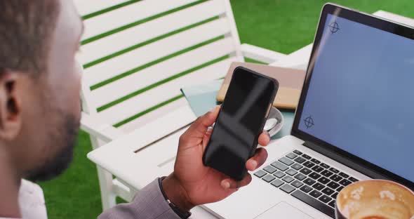 Midsection of african american businessman using smartphone and laptop in cafe alt