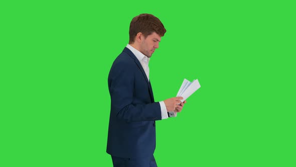 Serious Businessman Reading Documents or Report While Walking on a Green Screen, Chroma Key. alt