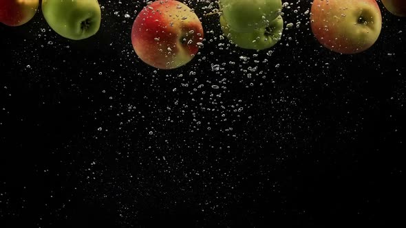 Red and Green Apples Falling in Splash of Water with Air Bubbles Isolated on Black Background alt