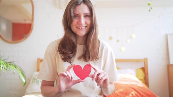 A Romantic Beautiful Woman with a Red Paper Heart in Her Hands Smiles and Looks Into the Camera