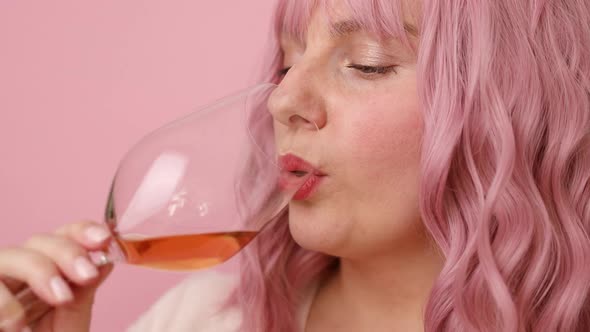 Beautiful 30s Woman with Pink Curly Hair Drinking Rose Wine Over Bright Pink Color Background alt