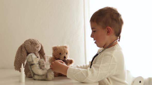 Cute little boy playing doctor at home and curing plush toy