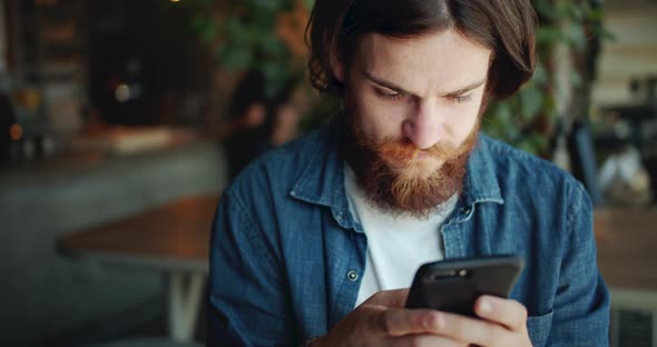 Male Hippie Texting on Smartphone in Cafe