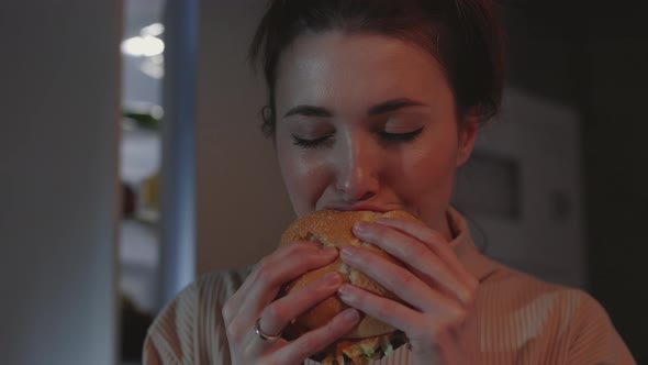 Woman Eating Burger at Night Near Refrigerator alt