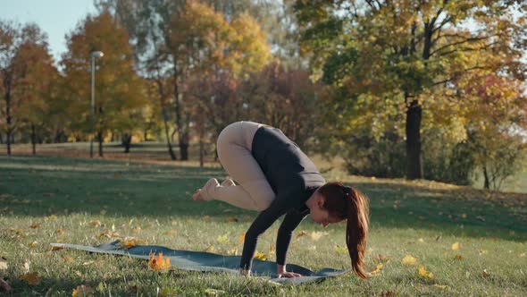 Young Woman Practices Active Yoga Standing on Hands in City Park on a Yoga Mat