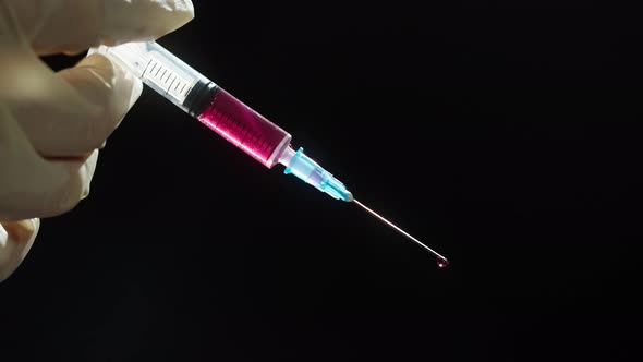 Hand in Protective Medical Gloves Holding Syringe with Red Solution on Black Background alt