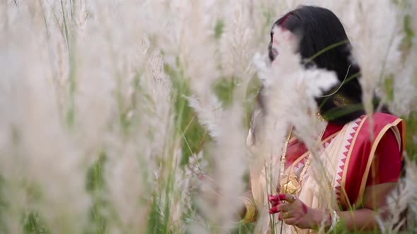 A happy and playful married Indian bengali woman wearing saree plays with the long white grass in a alt