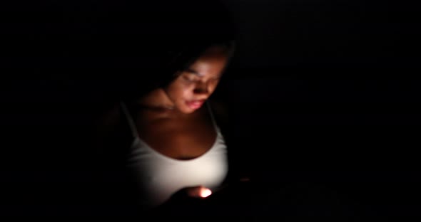 Black Woman use of mobile phone and lying on bed at night.