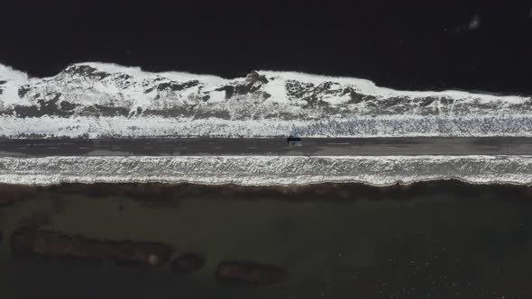 Bird's Eye View of a Car Driving Along a Narrow Road Crossing a Lake alt