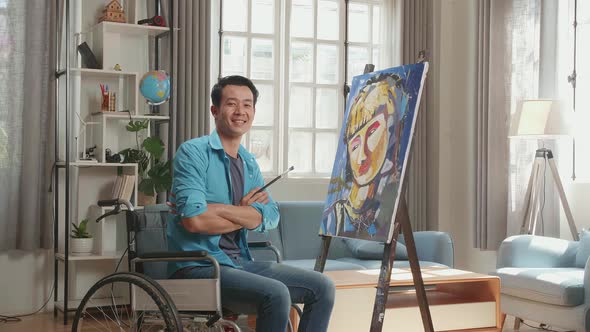 Asian Artist Man In Wheelchair Turn To Cross His Arms And Smile While Painting A Girl On The Canvas alt