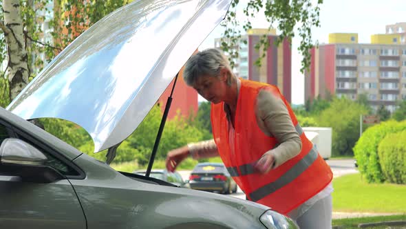 Middle Aged Woman Wears Warning Vest, Controls Engine of the Car and She Doesn't Know What To Do alt