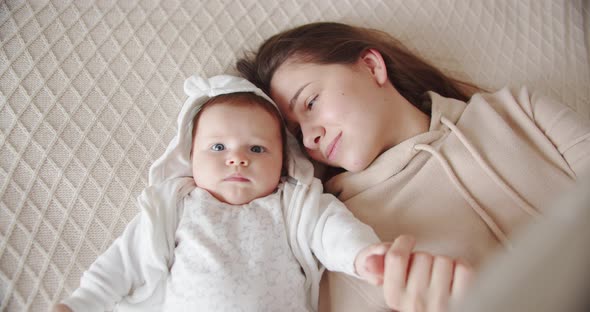 Newborn Baby Holds Mom's Hand While Lying On The Bed