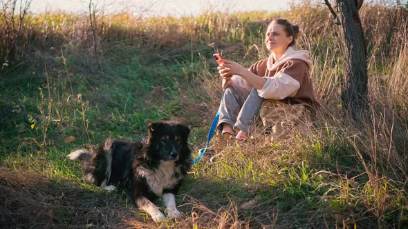 A Young Adult Woman Using Her Phone While Walking with Her Dog alt