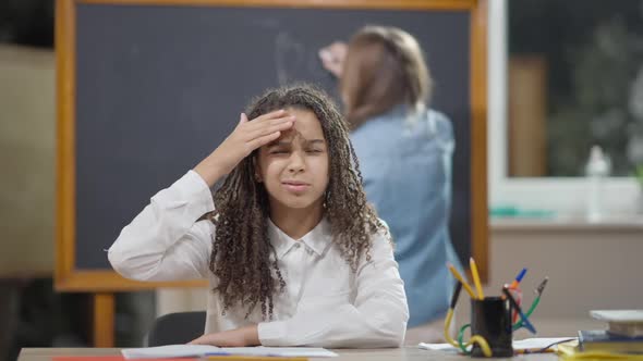 Portrait of Sad Exhausted African American Schoolgirl Falling Asleep Sitting at Desk in Classroom alt