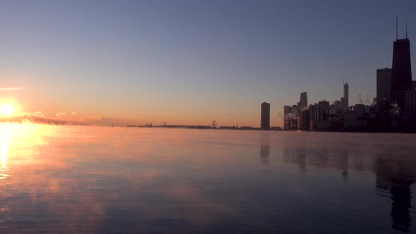 Sun rising over Lake Michigan horizon over Chicago downtown skyline in winter with sea smoke in wate alt