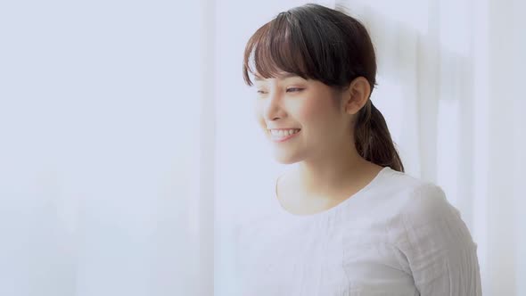 Beautiful young asian woman looking out of window in bedroom at morning after wake up. alt