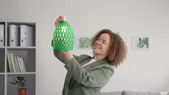 Modern Technologies Young Woman Designer is Decorating Room and Hangs 3D Printed Lamp Shade Smiles alt