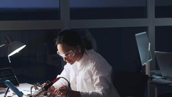 African American Electronics Specialist in Protective Glasses and White Coat Working with Multimeter alt