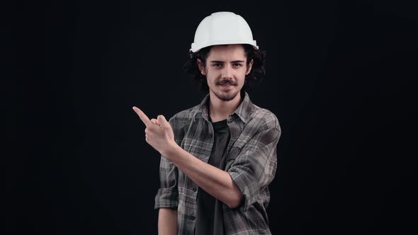 The Charismatic Hipster with the Engineer's White Helmet Looks Cheerful with His Index Finger to One alt