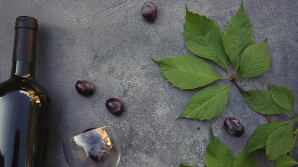 Top View of Bottle of Red Wine Green Vine Wineglass and Ripe Grape on Vintage Dark Stone Table alt