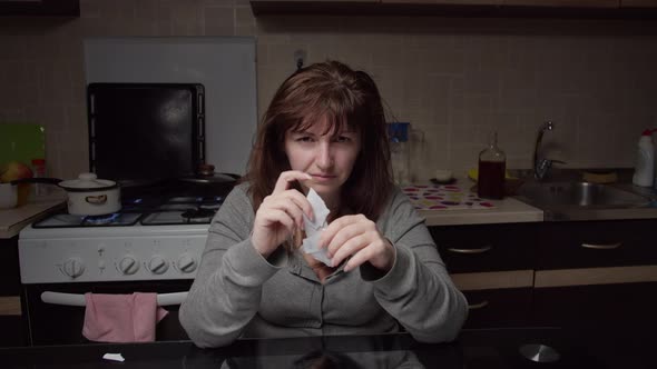 Sad Woman Sits in the Kitchen and Tears a Letter Into Small Pieces in the Evening, Bad Mood