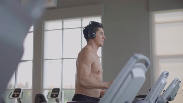 Athletic man listening to music and walking on treadmill