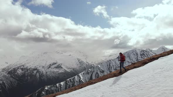 Aerial View Young Man in Sunglasses with a Backpack Goes Down the Mountain on the Crest on the alt