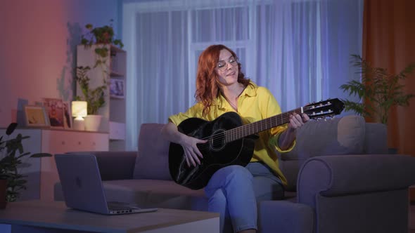 Woman Playing an Instrumental Guitar Studying Music and Notes on Laptop While Sitting on Couch at