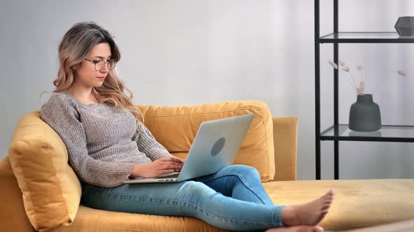 Focused Freelancer Female Working Remotely Use Laptop Relaxing on Yellow Couch alt
