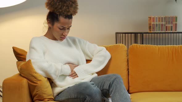 Young Black Woman Suffers From Abdominal Pain on the Couch at Home alt