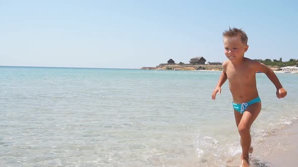 On the Azure Sea Water Runs a Blond Cute Boy on a Sunny Cloudless Day Slowmotion Video