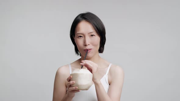 Mature Japanese Woman Drinking Coconut Water With Straw Gray Background alt