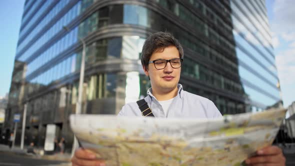 Pan Shot of Man with Map Standing in the Center of the Roading Looking at the Buildings alt