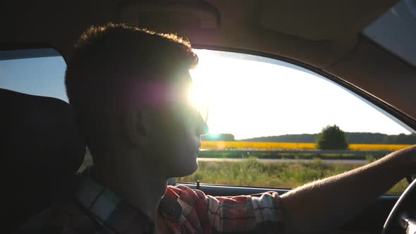Profile of Young Man in Sunglasses Driving a Car with Sun Flare at Background alt