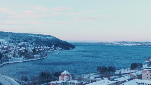 Wide aerial rise from city of Östersund towards waters on winter day alt