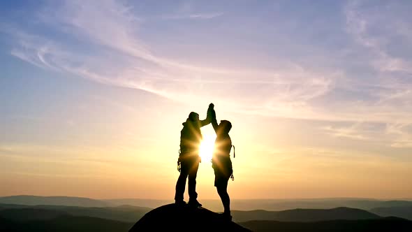 Silhouettes of a Young Couple Happily Shaking Hands and Embracing on a Mountaintop at Sunset