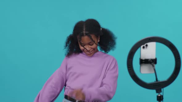 Young African Girl Dances on a Blue Light Background and Takes a Selfie Video on Smartphone for a alt