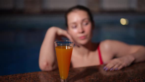 Closeup Refreshing Cocktail on Poolside with Young Blurred Woman in Water at Background alt