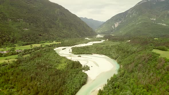 Aerial view of Soca river surrounded by a small town and many hills in Slovenia. alt