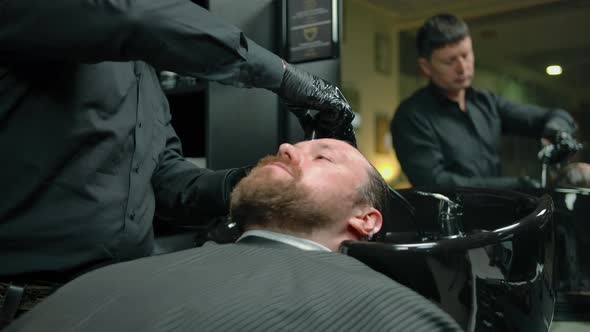 Bearded Man Washed with Shampoo Foam in a Barbershop By Professional Barber alt