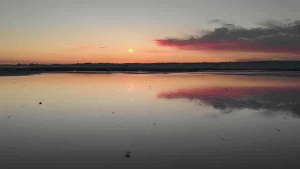 flying backward above a reflecting sunset over a salt lake revealing a couple