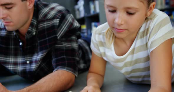 Schoolgirl lying on floor and reading book in classroom alt