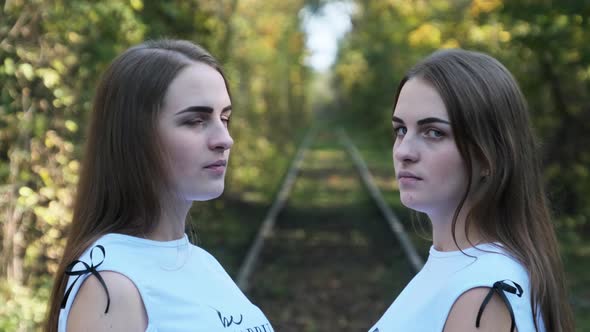 Twins Girls on Railroad Look at Camera in Green Nature Background. Slow Motion alt