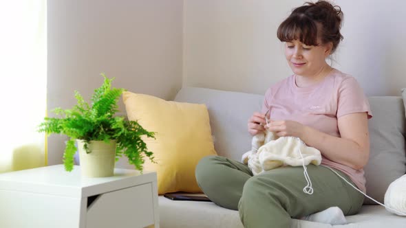 Young Woman Knitting White Knitwear on Sofa at Home alt