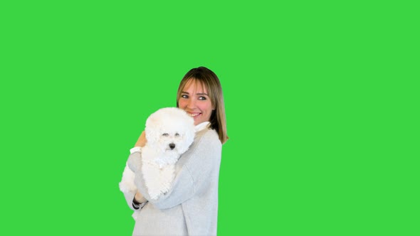 Charming Girl Standing with Bichon Frise in Her Hands on a Green Screen Chroma Key