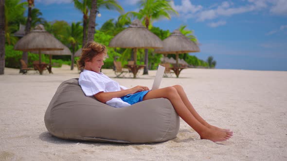 A Student is Engaged in Selfeducation Sitting on the Beach Against the Background of the Turquoise alt
